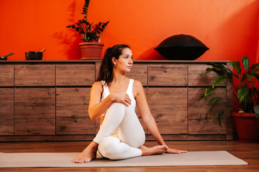 Beautiful young woman in white sports clothes is sitting on yoga mat
